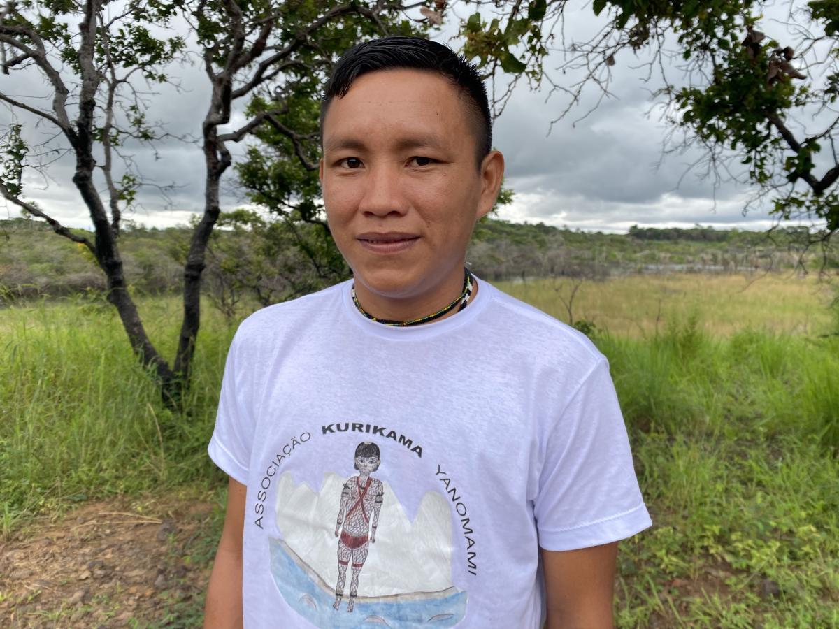 Roni Raitateri Yanomami, Tesoureiro da Associação Kurikama Yanomami, posa para foto usando uma camiseta branca. Ao fundo, tem uma área verde